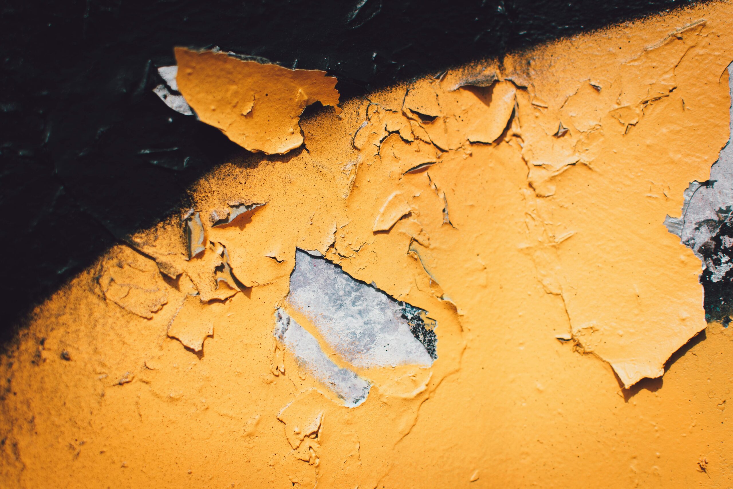 A detailed close-up of peeling yellow paint on a textured wall with visible decay.