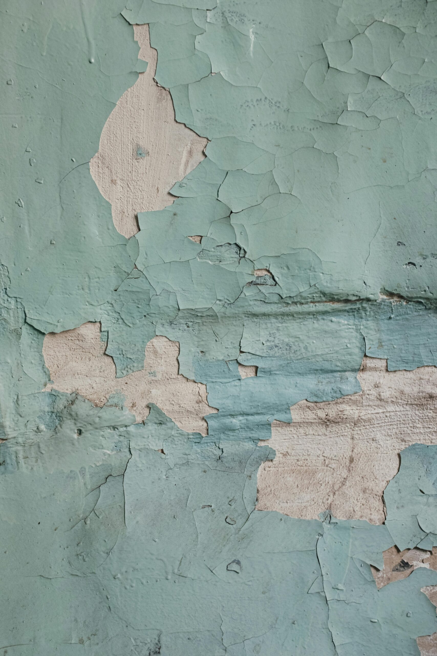 Close-up of peeling blue paint on an aged, textured wall, showing decay and roughness.